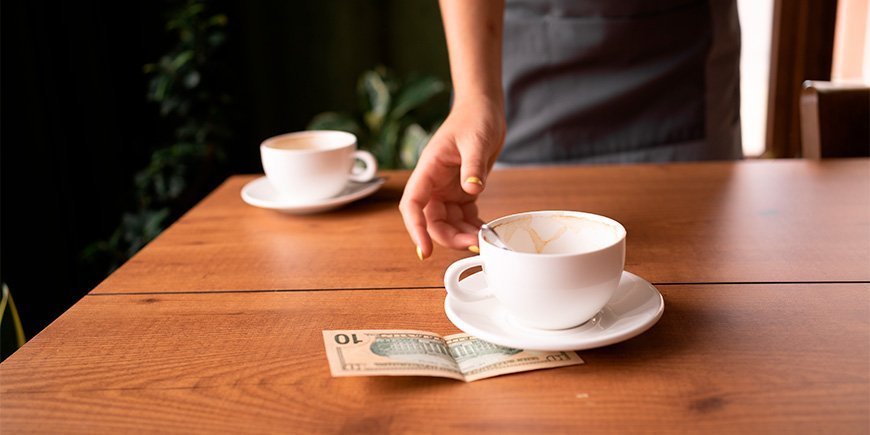 Kellner nimmt eine Tasse und Trinkgeld von einem Tisch in einem Café