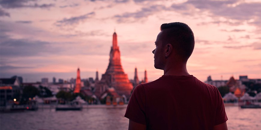 Mann steht bei Sonnenuntergang vor dem Wat Arun in Thailand