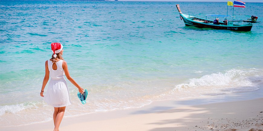 Frau geht am Strand in Thailand mit Weihnachtsmannmütze spazieren