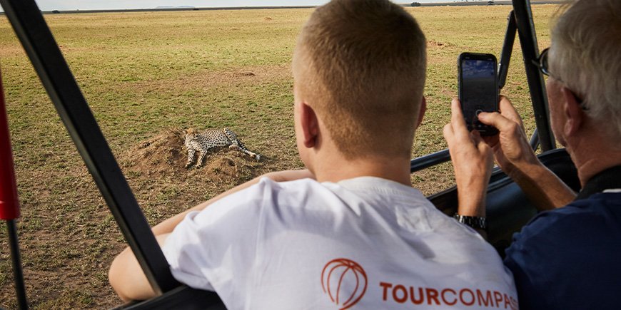 Zwei Männer betrachten einen Geparden, der in der Savanne der Serengeti liegt